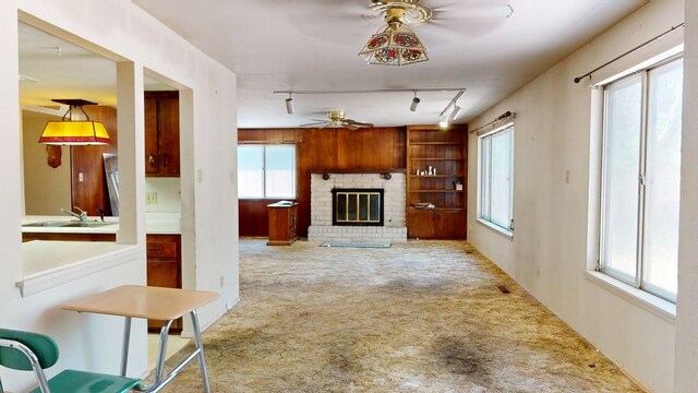 carpeted living area with rail lighting, a ceiling fan, a sink, and a fireplace