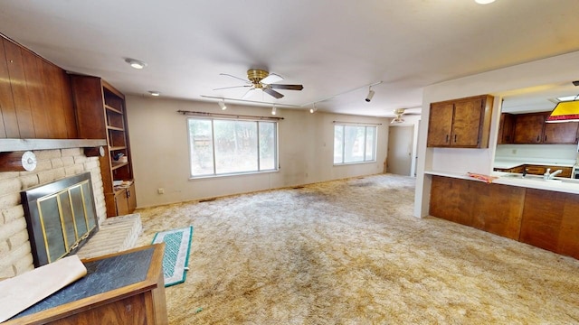 unfurnished living room with a ceiling fan, carpet flooring, rail lighting, and a brick fireplace