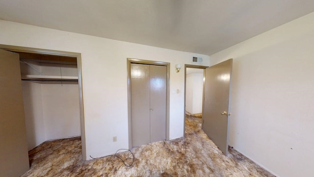 unfurnished bedroom featuring carpet, visible vents, and two closets