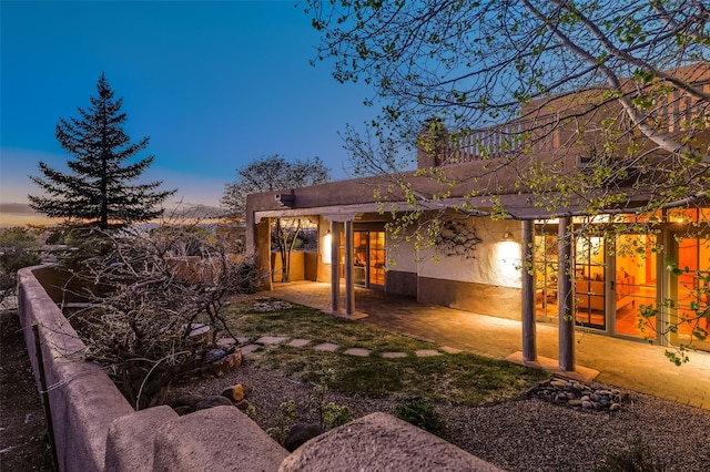back of house at dusk featuring a chimney, a patio, and stucco siding