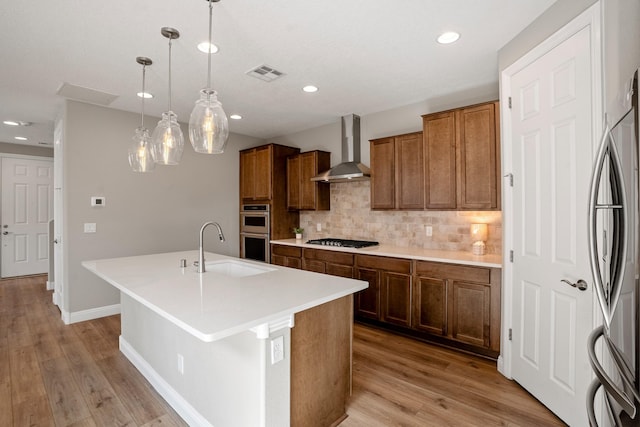 kitchen featuring a sink, visible vents, backsplash, wall chimney range hood, and appliances with stainless steel finishes