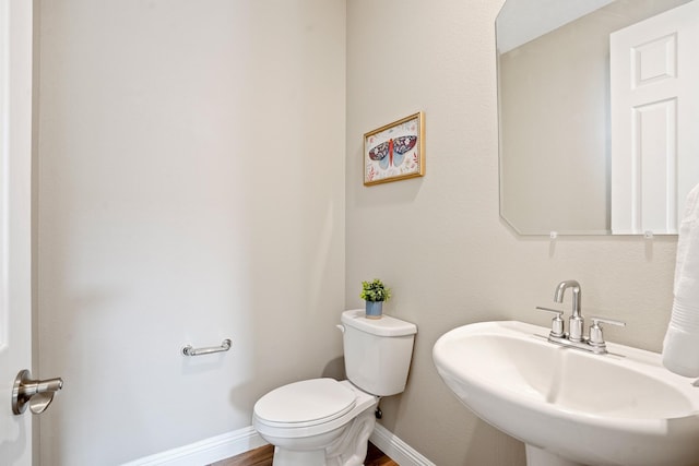 bathroom featuring baseboards, wood finished floors, toilet, and a sink