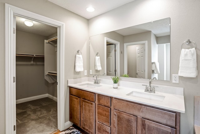 full bathroom with a walk in closet, double vanity, a sink, and baseboards