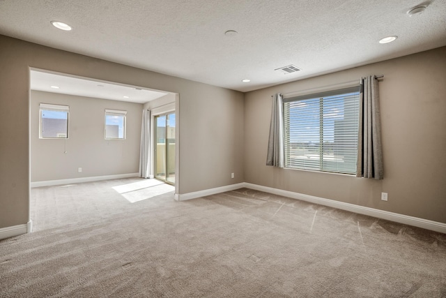 carpeted spare room featuring a textured ceiling, visible vents, and a healthy amount of sunlight