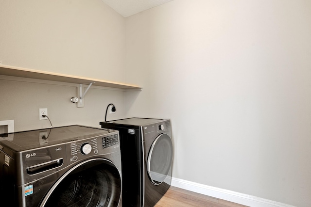 washroom featuring baseboards, washer and clothes dryer, light wood-style floors, and laundry area