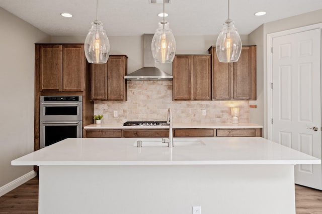 kitchen with stainless steel appliances, light countertops, wood finished floors, and wall chimney range hood