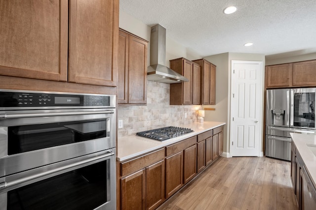 kitchen featuring tasteful backsplash, stainless steel appliances, light wood-style floors, light countertops, and wall chimney exhaust hood