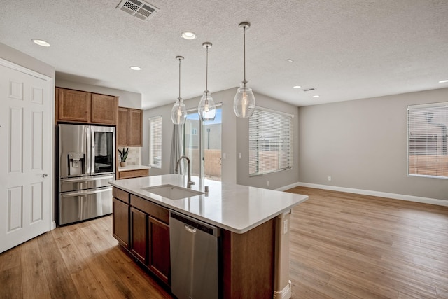 kitchen featuring stainless steel appliances, decorative light fixtures, light wood-type flooring, a sink, and visible vents