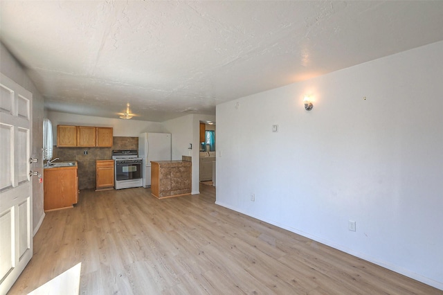 kitchen with light wood finished floors, tasteful backsplash, baseboards, gas range oven, and freestanding refrigerator