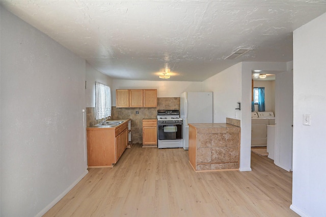 kitchen with range with gas cooktop, light wood-style floors, washing machine and clothes dryer, and freestanding refrigerator