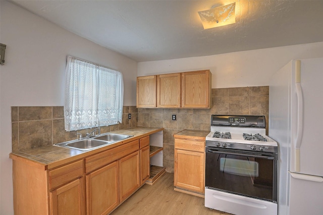 kitchen featuring a sink, light wood-style floors, freestanding refrigerator, gas stove, and tile countertops
