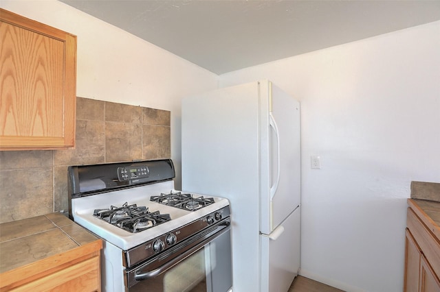 kitchen featuring tile counters, light brown cabinets, freestanding refrigerator, and gas stove