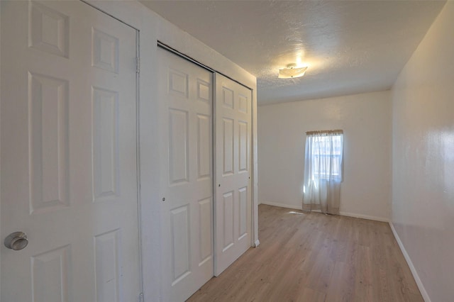 hallway with a textured ceiling, light wood finished floors, and baseboards