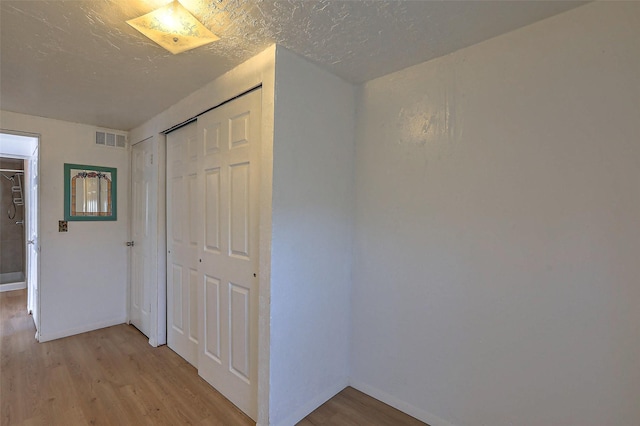 hallway with visible vents, light wood-style flooring, and baseboards