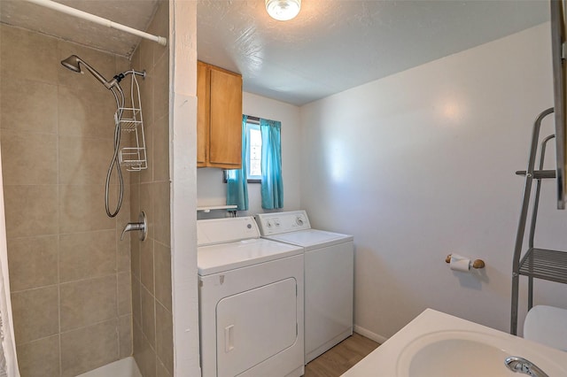 bathroom with a tile shower, a sink, baseboards, separate washer and dryer, and wood finished floors