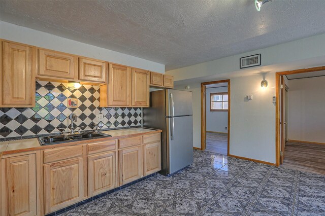 kitchen with freestanding refrigerator, backsplash, a sink, visible vents, and a textured ceiling