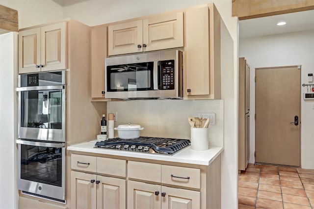kitchen with light tile patterned floors, decorative backsplash, stainless steel appliances, light countertops, and light brown cabinetry