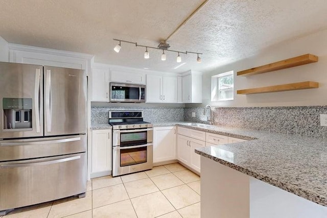 kitchen with a sink, light tile patterned floors, a textured ceiling, white cabinets, and appliances with stainless steel finishes