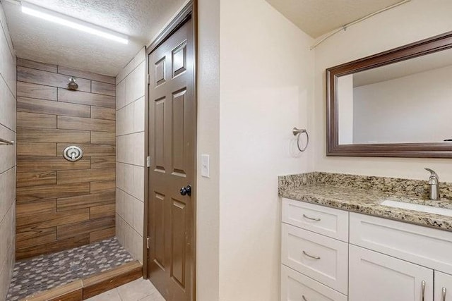 full bathroom featuring tile patterned flooring, a textured ceiling, tiled shower, and vanity
