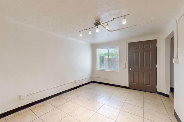 unfurnished room with light tile patterned flooring, a textured ceiling, and baseboards