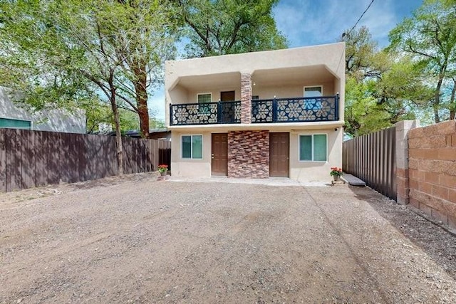 rear view of house featuring stucco siding, a fenced backyard, and a balcony