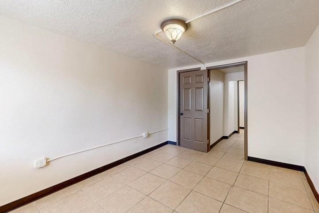 spare room featuring baseboards, light tile patterned floors, and a textured ceiling