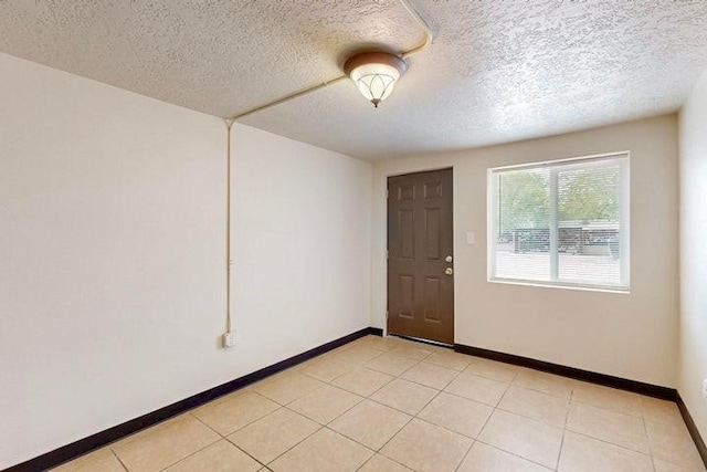 unfurnished room with baseboards, a textured ceiling, and light tile patterned flooring