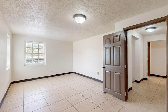 empty room featuring a textured ceiling, light tile patterned flooring, and baseboards