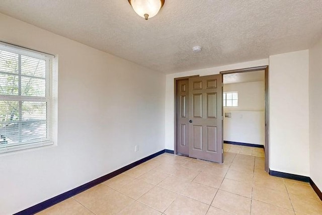 empty room with light tile patterned floors, a wealth of natural light, and baseboards