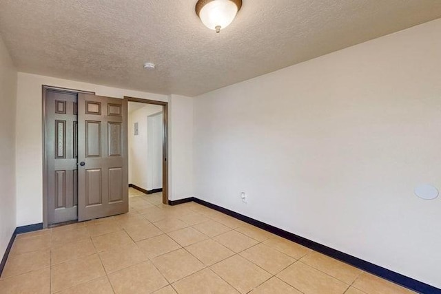 spare room featuring light tile patterned floors, a textured ceiling, and baseboards