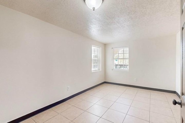 spare room with baseboards, light tile patterned floors, and a textured ceiling
