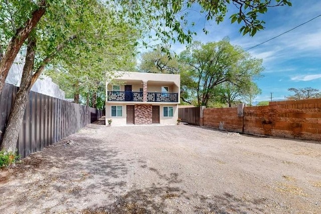 view of front of house featuring fence private yard, dirt driveway, stucco siding, and a balcony
