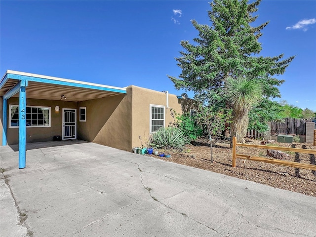 back of house featuring an attached carport, fence, concrete driveway, and stucco siding