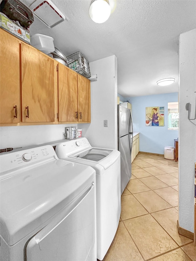 clothes washing area with a textured ceiling, cabinet space, light tile patterned floors, and washer and dryer