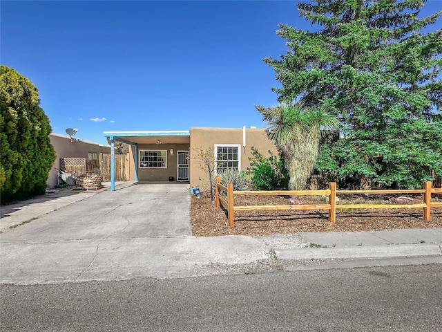southwest-style home with concrete driveway, a fenced front yard, an attached carport, and stucco siding