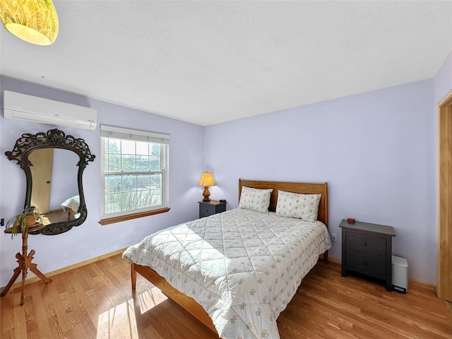 bedroom with baseboards, a wall mounted AC, and wood finished floors