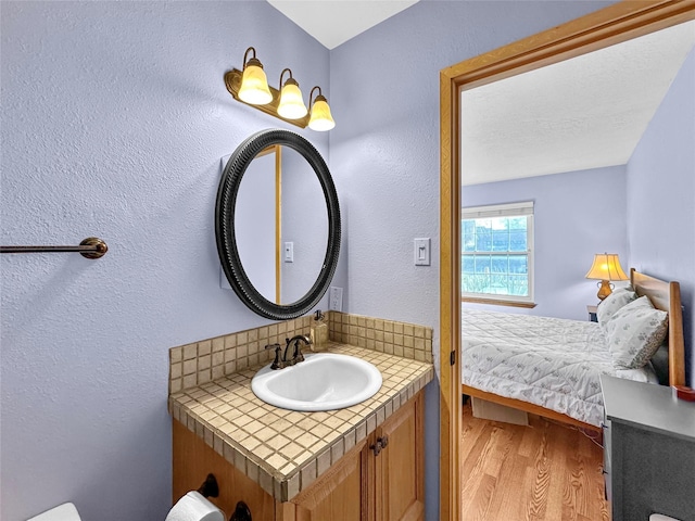 bathroom with vanity, a textured wall, wood finished floors, and tasteful backsplash