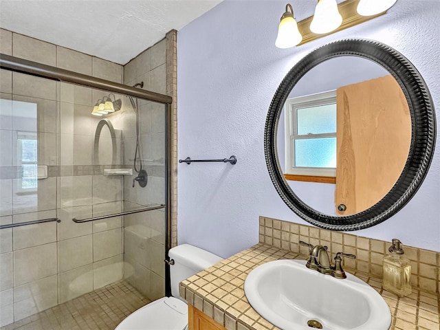 full bath with a textured wall, a sink, toilet, decorative backsplash, and a stall shower