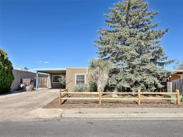 view of front facade with stucco siding, fence, an attached carport, and concrete driveway