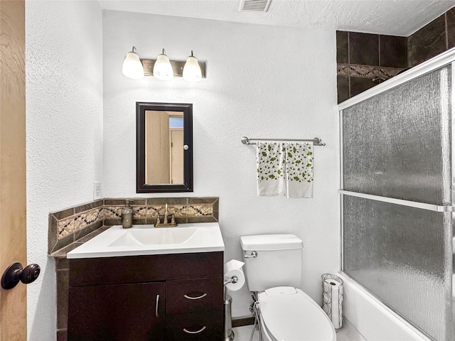 full bathroom featuring visible vents, vanity, toilet, shower / bath combination with glass door, and a textured wall