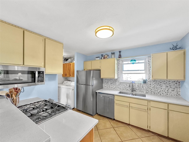 kitchen featuring appliances with stainless steel finishes, cream cabinetry, a sink, light countertops, and washer and clothes dryer