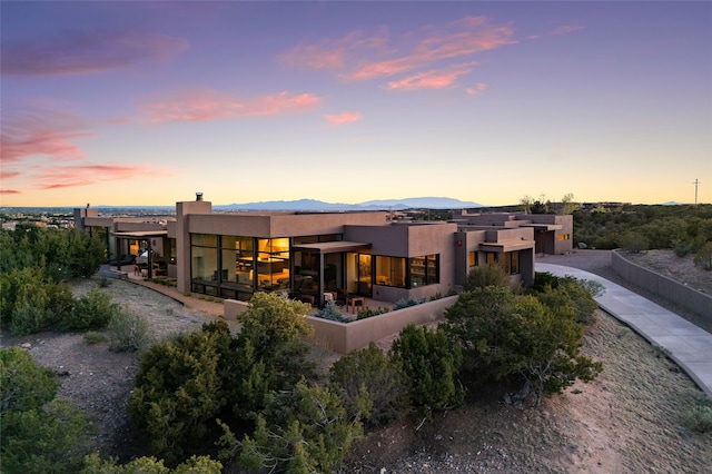 back of house at dusk with a mountain view, stucco siding, driveway, and a chimney