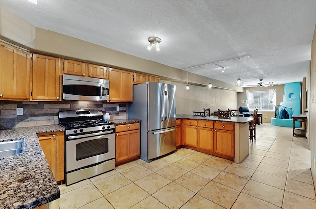 kitchen featuring light tile patterned flooring, a textured ceiling, stainless steel appliances, a peninsula, and decorative backsplash