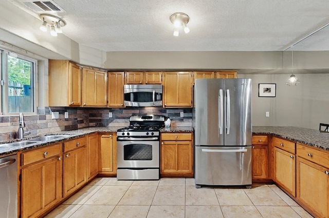 kitchen featuring dark stone countertops, appliances with stainless steel finishes, a sink, and tasteful backsplash
