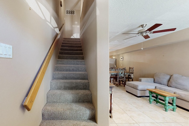 stairs with a textured ceiling, ceiling fan, visible vents, and tile patterned flooring