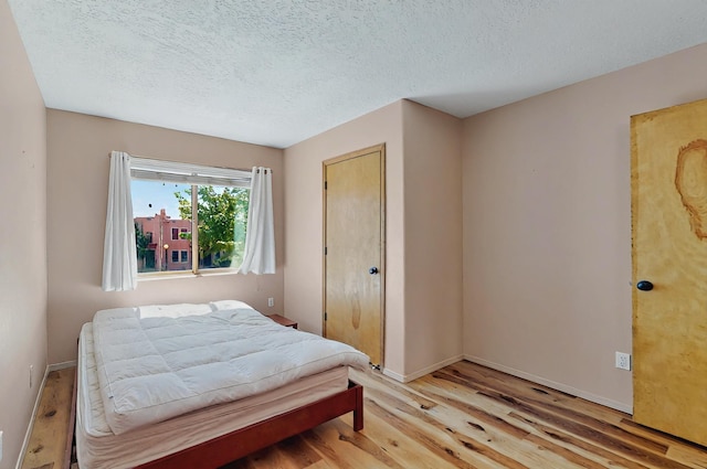 bedroom featuring baseboards, a textured ceiling, and wood finished floors