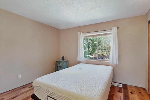 bedroom with baseboards, light wood finished floors, and visible vents