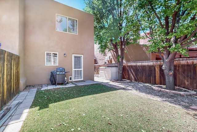 rear view of house featuring a lawn, a fenced backyard, and stucco siding