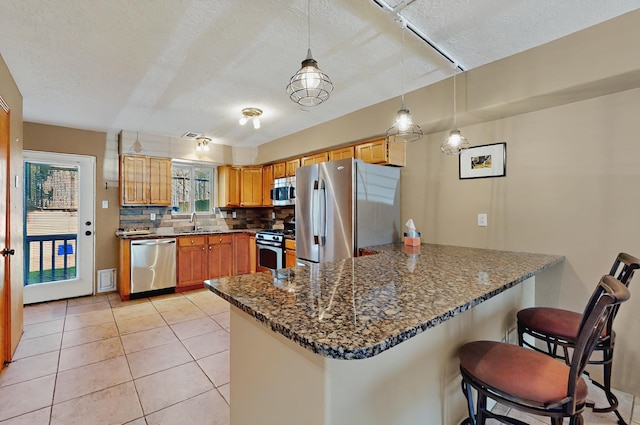 kitchen featuring a peninsula, a textured ceiling, tasteful backsplash, a sink, and stainless steel appliances