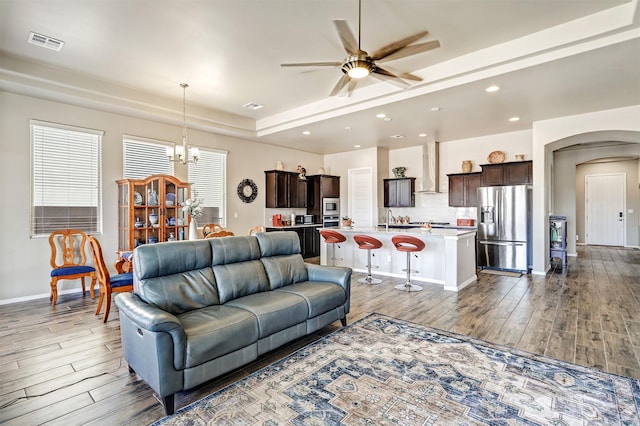 living room with visible vents, arched walkways, dark wood finished floors, ceiling fan with notable chandelier, and recessed lighting